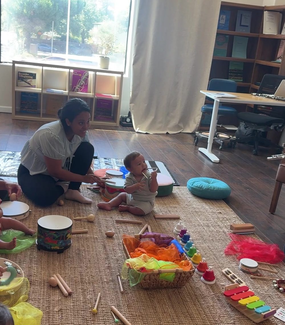A mom and her baby exploring instruments on the rug by the window