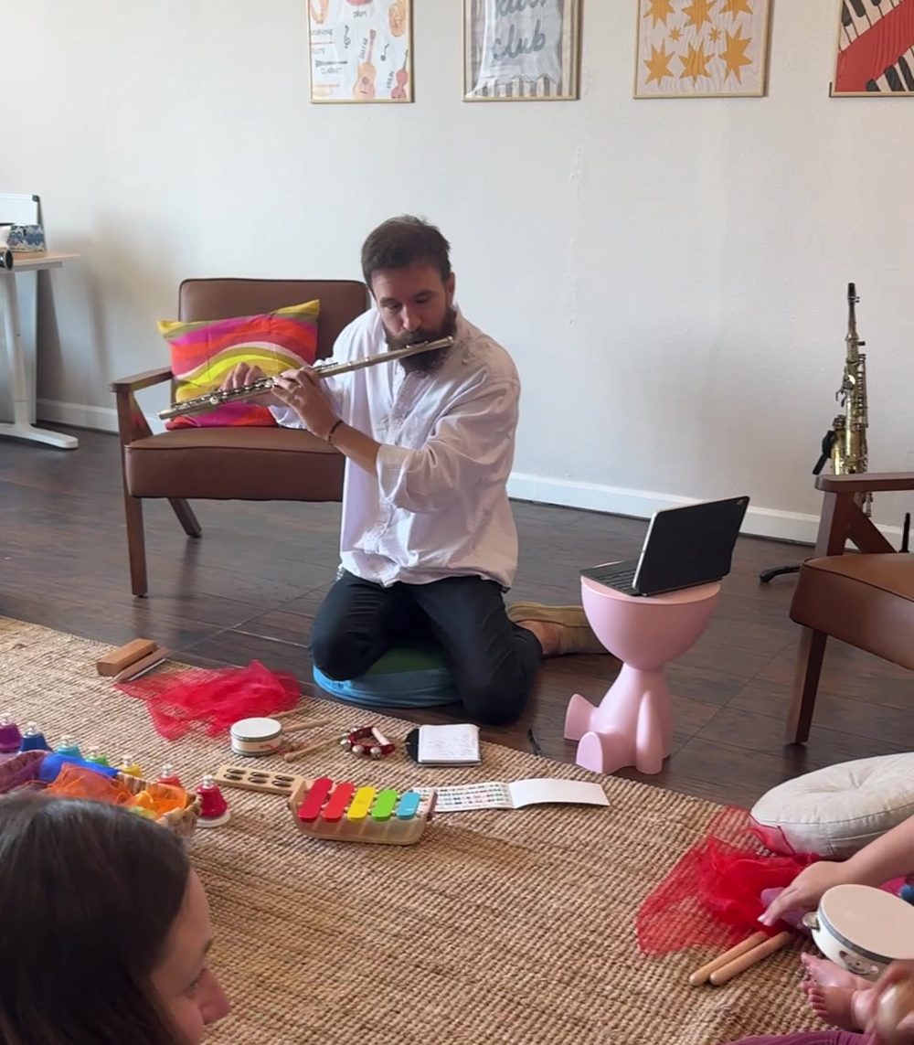 Claudiu Farcas kneeling on the rug, playing flute for the babies in class